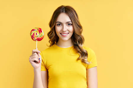 Happy beautiful woman with colorful lollipop on yellowの写真素材
