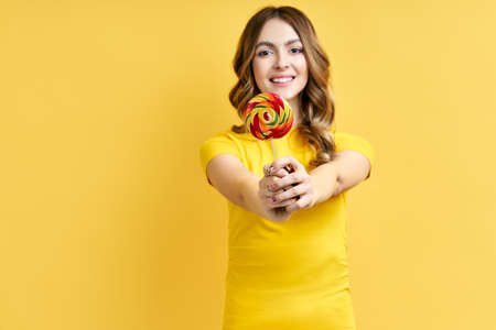 Happy beautiful woman with colorful lollipop on yellowの写真素材