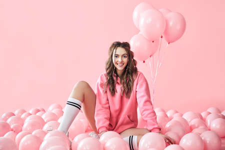 Young trendy woman posing with pink balloons on pink backgroundの写真素材