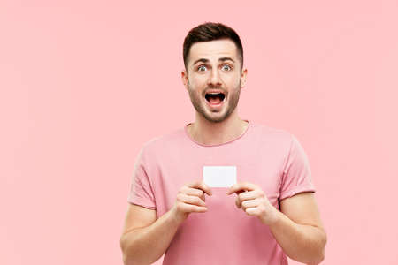 Amazed excited man with open mouth holding credit card over pink background