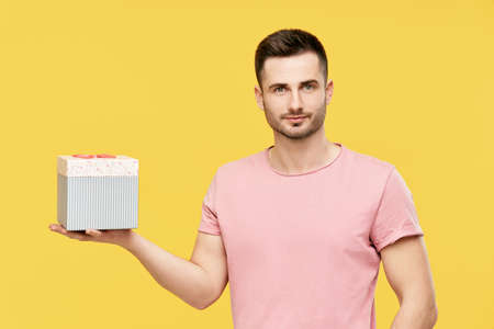 Handsome young man holding gift box on yellow studio backgroundの写真素材