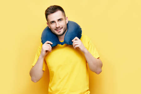 Young man with travel pillow on yellow backgroundの写真素材