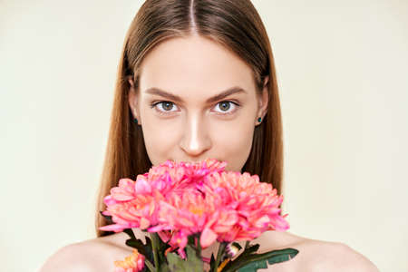 Portrait of beautiful young woman with flowers on studio backgroundの写真素材