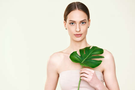 Young beautiful woman holding monstera tropical leaf with copy spaceの写真素材