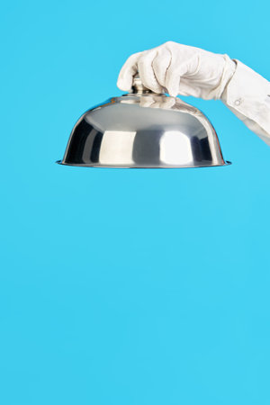Elegant waiters hand in white glove holding metal cloche lid cover on blue backgroundの写真素材