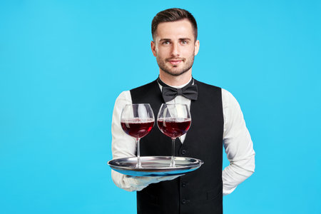 Elegant male waiter with glasses of wine over blue background