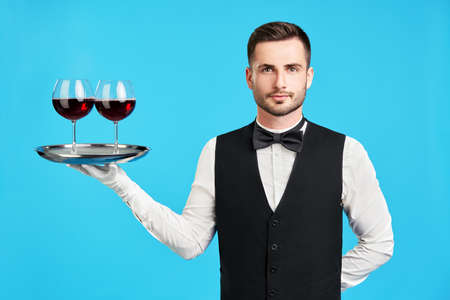 Elegant male waiter with glasses of wine over blue backgroundの写真素材