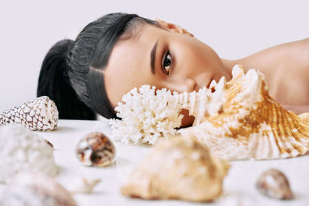 Fashion portrait of beautiful african american woman with different seashells looking through conch