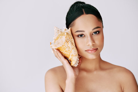 Pretty african american woman pressed conch seashell to her ear enjoy and dreamsの写真素材