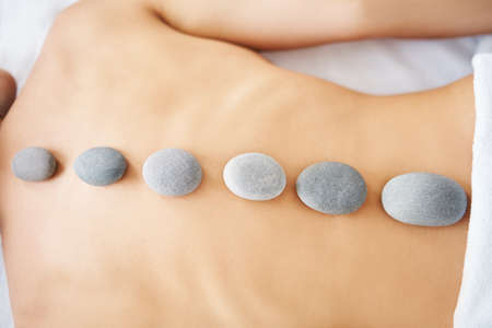 Cropped close up female relaxing in spa salon with hot stones on her backの写真素材