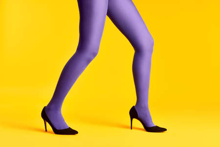 Female legs in purple tights and high heels shoes on yellow backgroundの写真素材