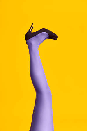 Raised females legs in bright tights and stylish high heels shoes on yellow backgroundの写真素材