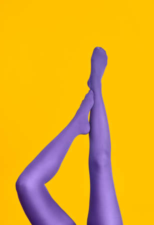 Slim female legs in purple tights raised up on yellow backgroundの写真素材