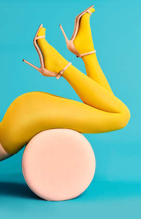 Legs of beautiful young woman wearing bright yellow tights and high heels shoes lying on poufの写真素材