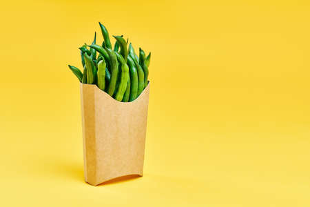 Fresh green beans in fast food paper box on bright yellow background with copy space