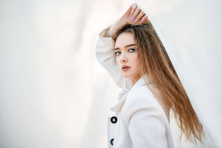Young attractive woman in white clothes posing on abstract pale background looking at camera confidentの写真素材