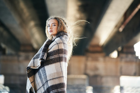 Portrait of pretty confident woman wrapped in wool blanket looking to camera posing on urban street background with copy spaceの写真素材