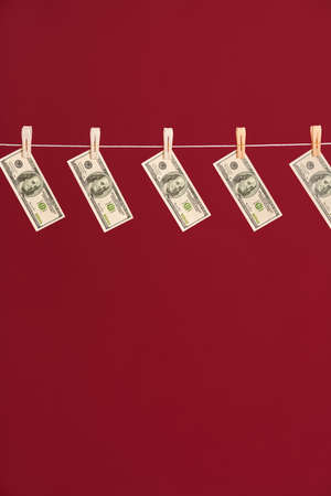 Money laundering, US dollars hanging on rope over red studio backgroundの写真素材
