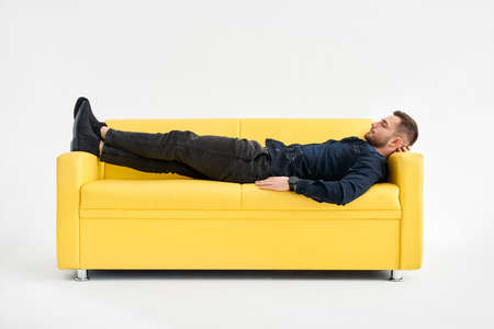Young man relaxing alone on yellow sofa at home