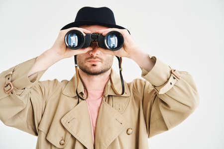 Young man wearing in coat and hat looking through binoculars over isolated white backgroundの写真素材