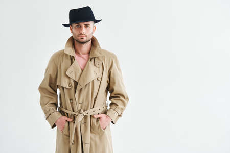 Young man in a trench coat and hat over white background with copy spaceの写真素材