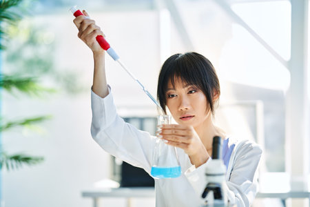 Female scientist making microbiology research using pipette, flask and test tubes working in modern chemical labの写真素材