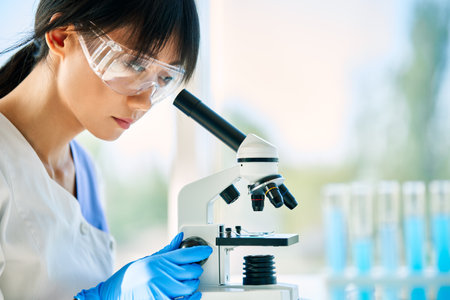 Portrait of asian scientist looking through a microscope working on medical research in modern...