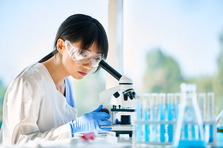 Portrait of asian scientist looking through a microscope working on medical research in modern...