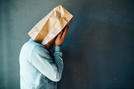 Upset man with a paper bag on head covering eyes with both hands. Profile view, copy spaceの写真素材