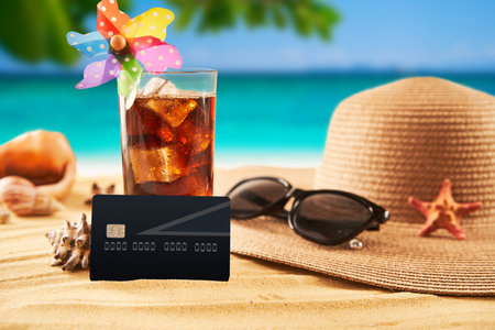 Travel concept. Credit card with straw hat, sunglasses and cocktail on on the sand and sea backgroundの写真素材