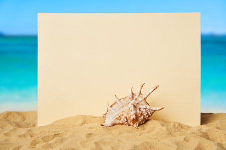 Blank paper with seashells and starfish on the sandy beach at ocean background. Summer time concept, vacation, card mockupの写真素材