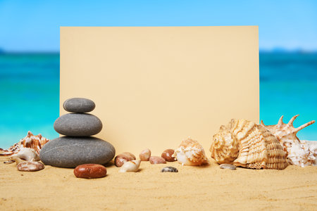 Invitation or greeting card mockup with seashells and pyramid of stones on the summer sandy beachの写真素材