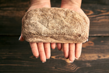 Loaf of fresh made rye multigrain bread in woman hands on wooden table background