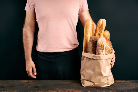 Man holds fresh loaves of bread baguettes in paper bag over light backgroundの写真素材