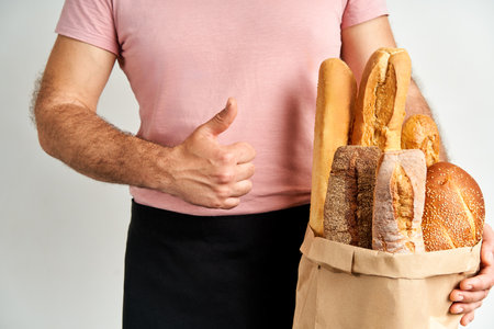 Man holds fresh loaves of bread baguettes in paper bag over light backgroundの写真素材