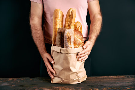 Man holds fresh loaves of bread baguettes in paper bag over light backgroundの写真素材