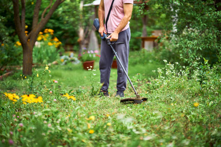 Close up of young man cutting grass with weed cutter on his grassy lawn.