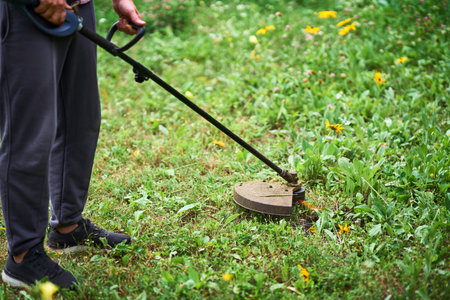 Close up of young man cutting grass with weed cutter on his grassy lawn.