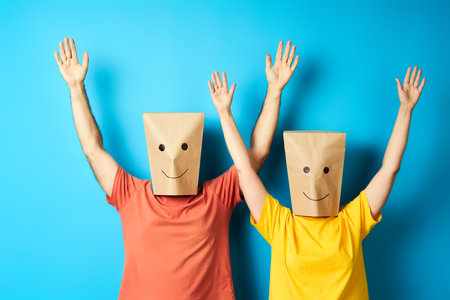 Happy smiling couple with bags over heads celebrating success with winner gestureの写真素材