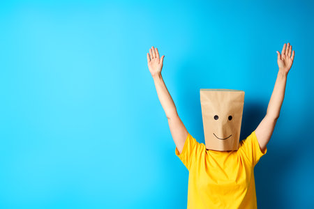 Woman with happy smile on the paper bag on head celebrating success with winner gestureの写真素材