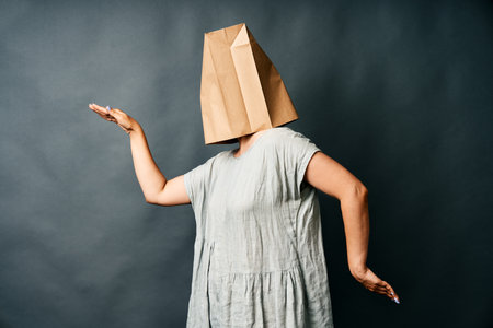 Woman with paper bag over her head dancing on dark background.の写真素材