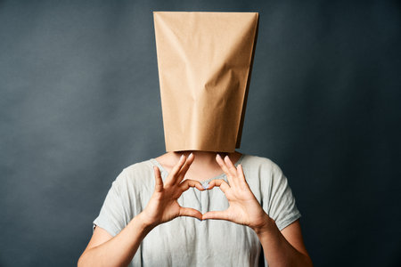 Woman with paper bag over her head making heart shape with hand.の写真素材