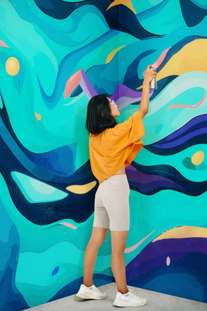 Female street artist painting bright colorful graffiti on wallの写真素材
