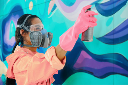 Female street artist painter in respirator mask painting colorful graffiti on wallの写真素材