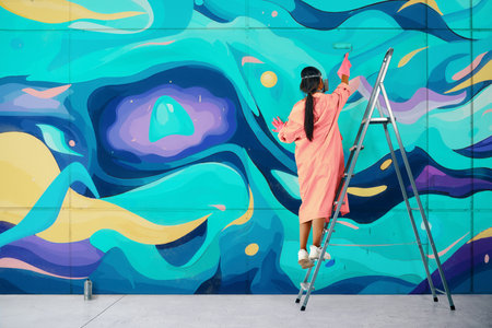 Female street artist painting colorful graffiti standing on a ladder using paint rollerの写真素材