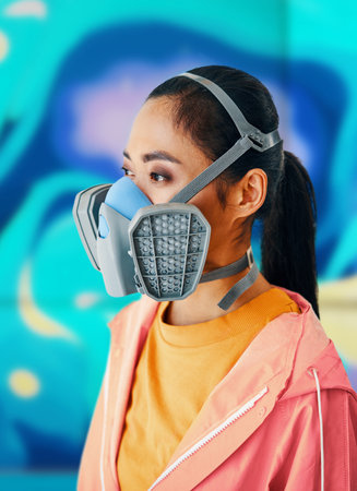 Close up portrait of graffiti street artist in respirator mask standing near the wall with her colorful paintings. Urban art conceptの写真素材