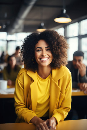 Pretty young black woman with curly hair smiling wearing bright yellow blazer at casual office. Generative AIの素材