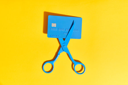 Blue scissors cutting credit card on bright yellow background. Finance conceptの写真素材