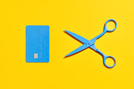 Blue scissors and credit card over yellow background. Flat lay