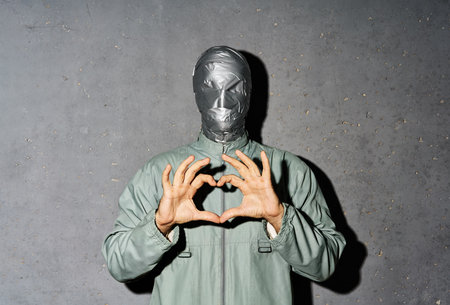 Mystery man making heart shape with hands over gray background